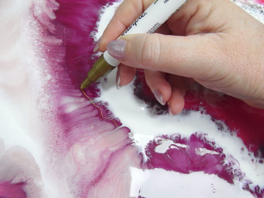 Hand drawing gold veins on a pink and white resin painting