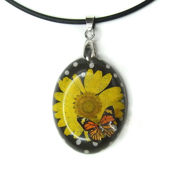 Oval shaped resin pendant filled with yellow daisy on a black and white polka dot background. A resin butterfly is attached to the bottom of the cabochon