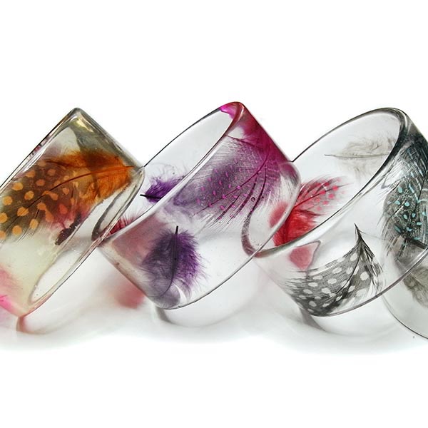 Three clear resin bangles filled with colourful feathers