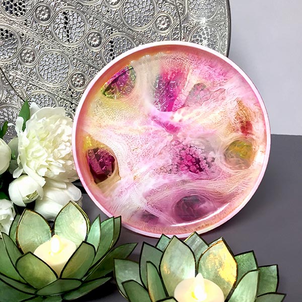 pink, yellow and white round resin platter displayed in front of 2 green lotus candle holders and a silver platter
